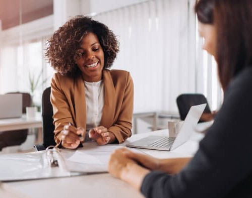 Woman sitting at a desk speaking with another woman